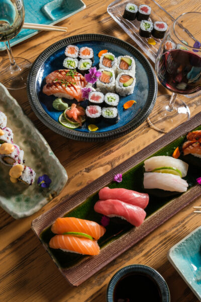 From above of assorted tasty sushi rolls with raw tuna and salmon served with wineglass with red wine on table